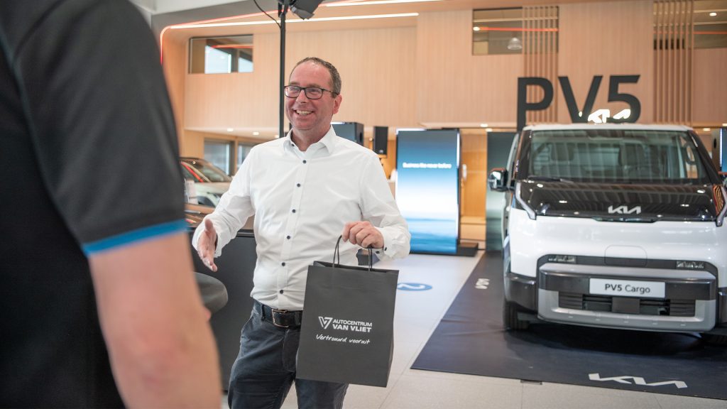 Verkoopadviseur schudt hand met klant na aankoop Kia PV5