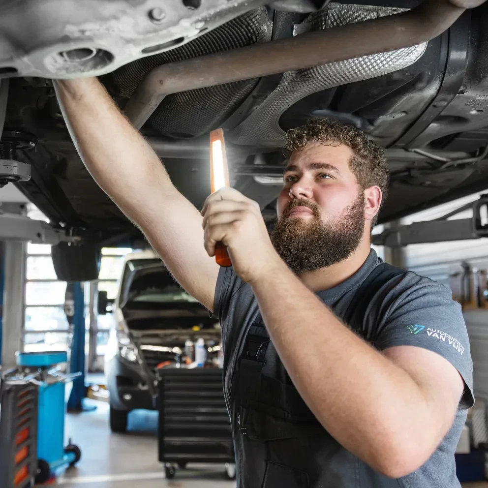 Een monteur inspecteert een auto op een hefbrug met een werklamp in de werkplaats.