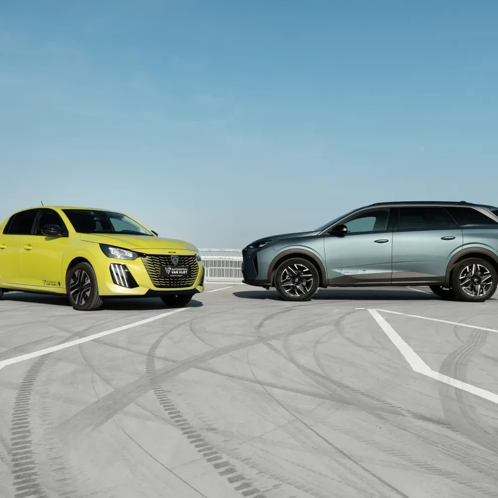 Een Peugeot E-208 en een Peugeot 5008 staan geparkeerd op een parkeerplaats.