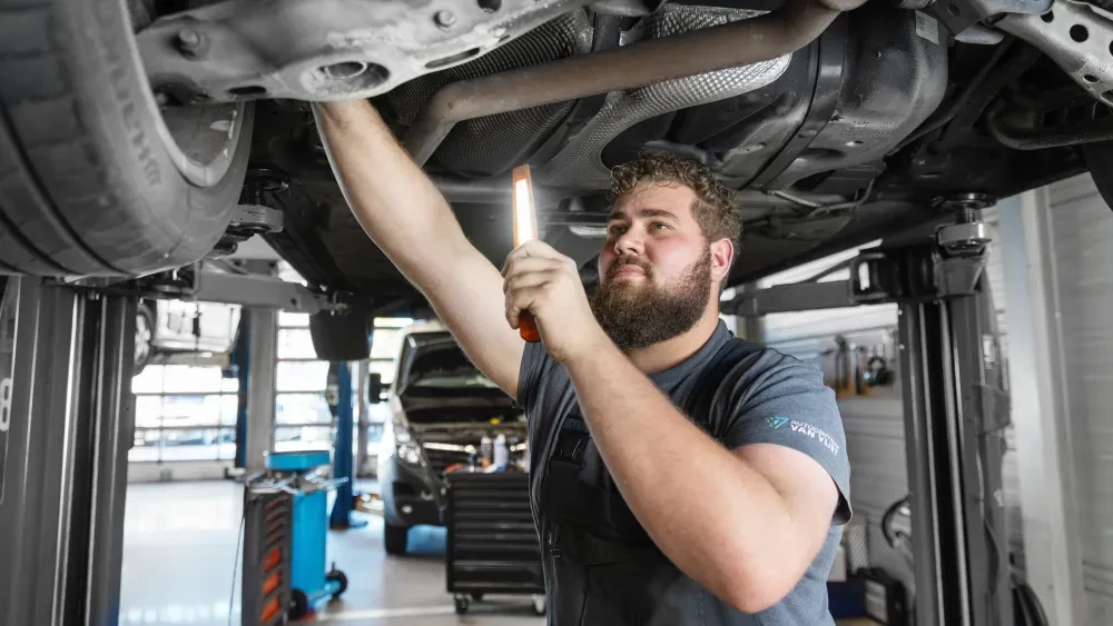 Een monteur inspecteert een auto op een hefbrug met een werklamp in de werkplaats.