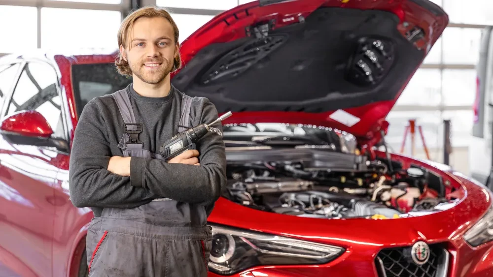 Monteur staat naast een rode Alfa Romeo met een schroeftol in zijn hand