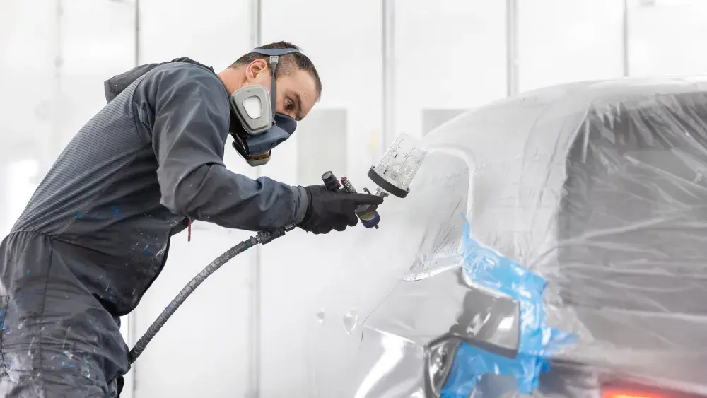 De autospuiter brengt een nieuwe laklaag aan op een auto-onderdeel.