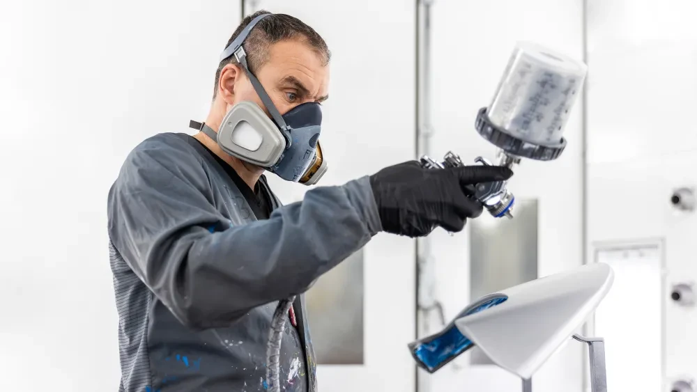 De autospuiter brengt een nieuwe laklaag aan op een auto-onderdeel.