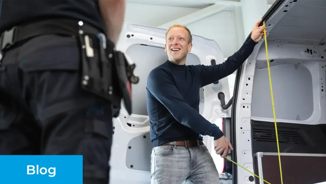 Verkoopadviseur geeft advies bij het kopen van een bedrijfswagen. Hij is de laadruimte van een witte bedrijfswagen aan het opmeten.